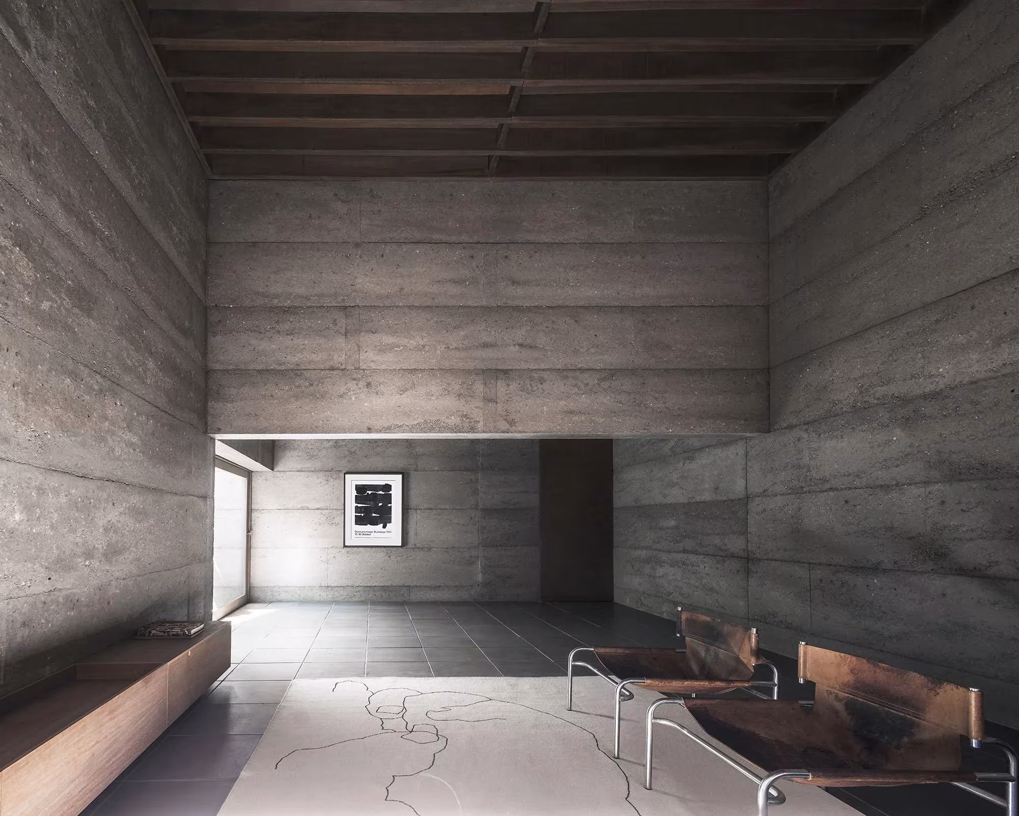 Salón de hormigón visto con butacas de cuero, banco corrido y un cuadro enmarcado en Cloister House