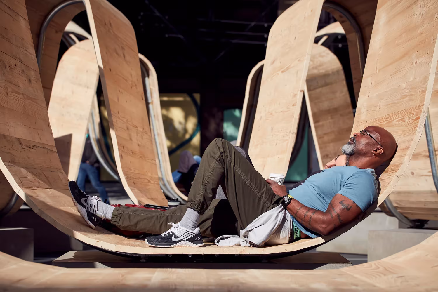 Hombre tumbado en la curva de madera de Please Be Seated, que sirve de asiento en Londres
