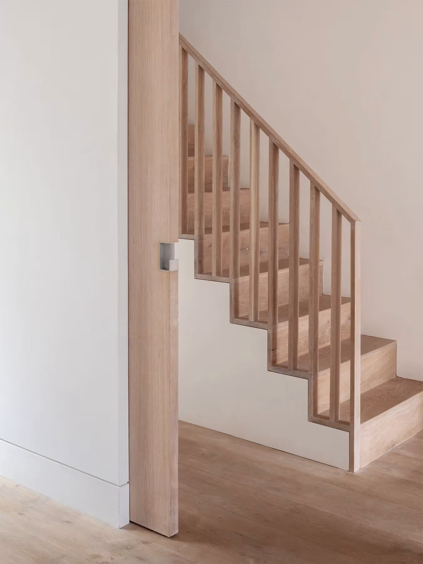Escalera de madera clara con barandilla de listones verticales junto a una pared blanca en Kings Grove