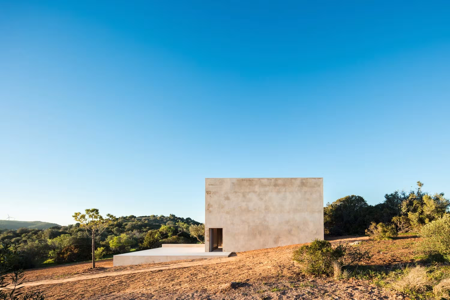 Capilla de piedra caliza de Siza sobre un plinto blanco entre el monte bajo del Algarve