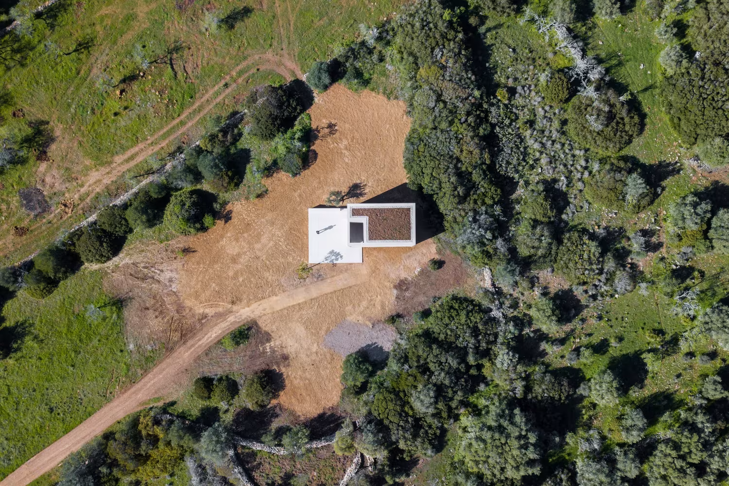 Vista aérea de la Capela do Monte, volumen blanco aislado entre vegetación y caminos de tierra, Algarve