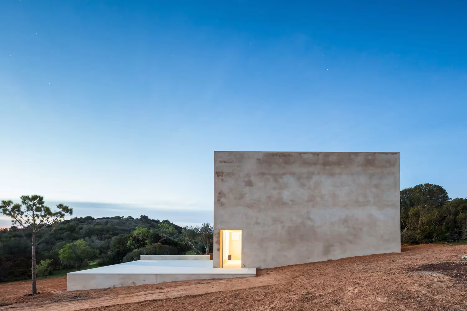 Capela do Monte de Álvaro Siza con la puerta iluminada en su cara de piedra y el plinto blanco