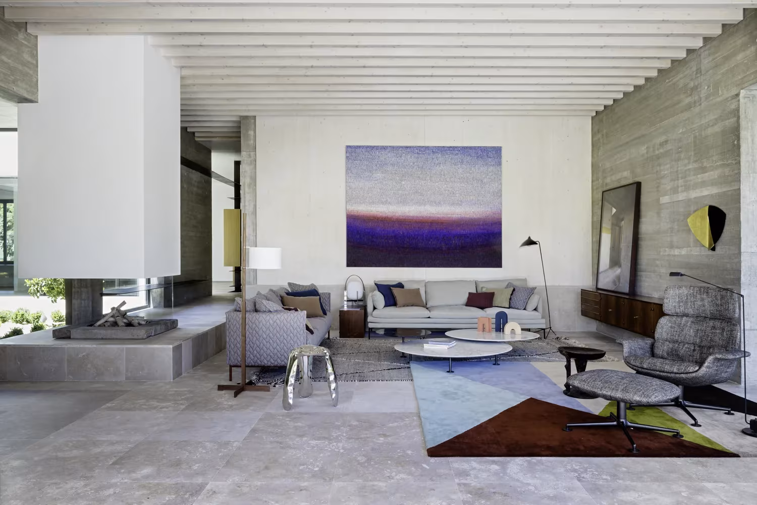 Salón con muro de hormigón visto, chimenea blanca suspendida y alfombra de colores en el Proyecto AS