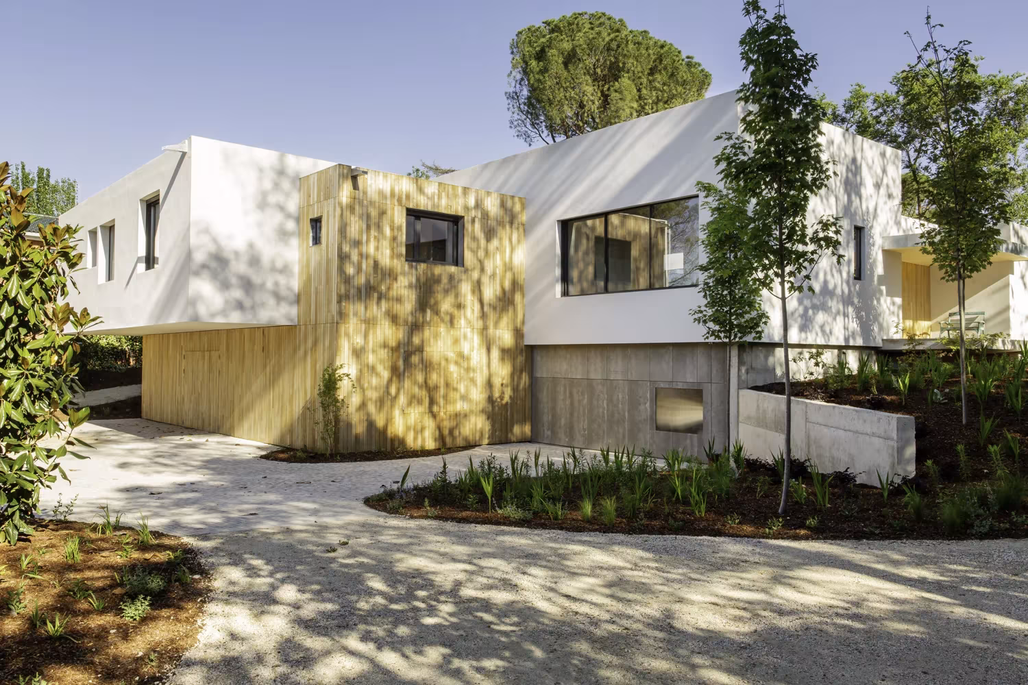 Fachada de la vivienda con volúmenes blancos y revestimiento de madera entre árboles, Proyecto AS en Madrid