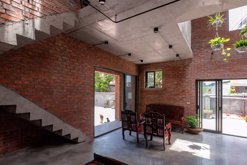 Salón con escalera, muros de ladrillo y puertas correderas al exterior en la casa AgriNesture, Vietnam