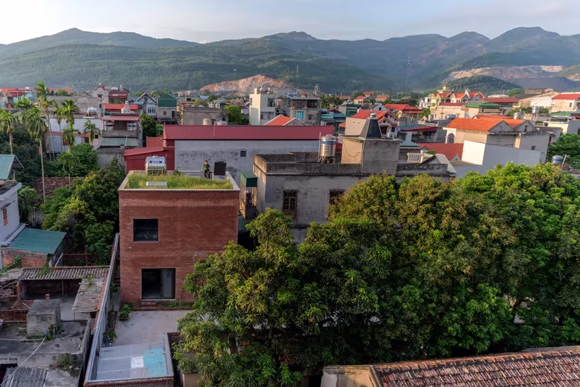Vista elevada de AgriNesture, casa de ladrillo con cubierta ajardinada entre tejados y montañas de Vietnam