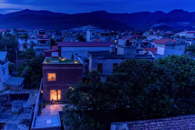 Casa AgriNesture iluminada al anochecer entre tejados y montañas del Vietnam rural