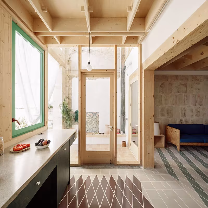 Cocina y paso acristalado con carpintería verde y pavimento de baldosas en rombos en la Plywood House, Palma
