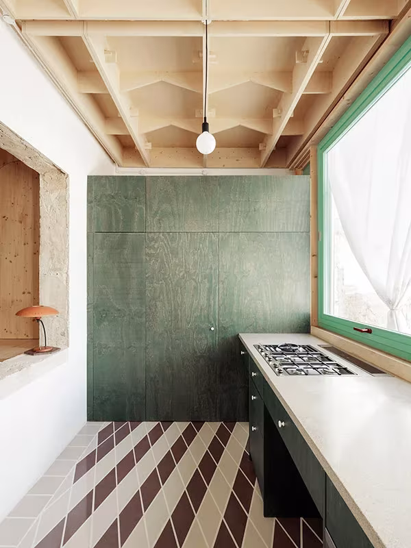 Cocina con panel de contrachapado verde, encimera blanca y ventana junto al techo de madera, Plywood House