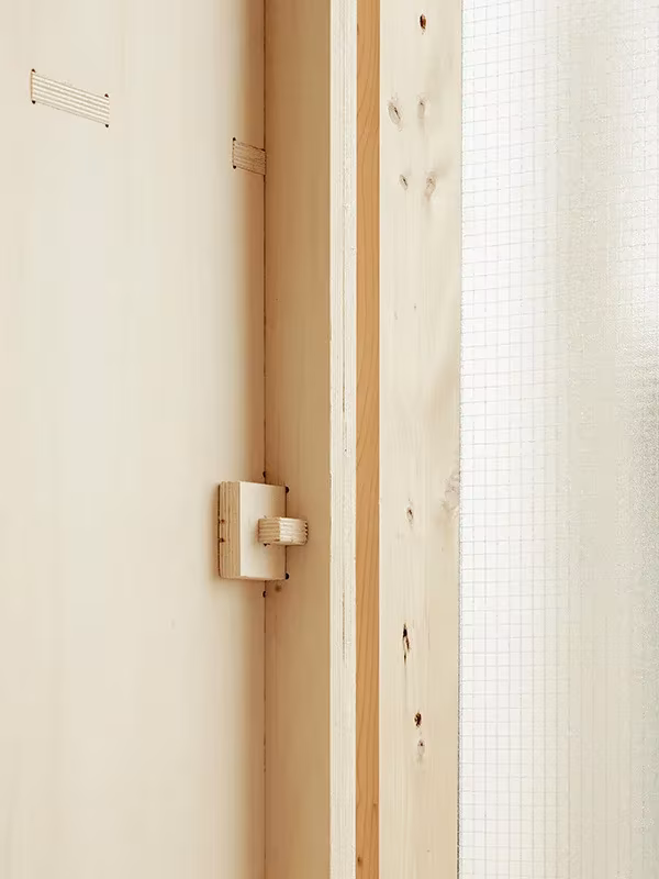 Detalle de un pestillo de madera entre montantes de pino y vidrio translúcido en la Plywood House