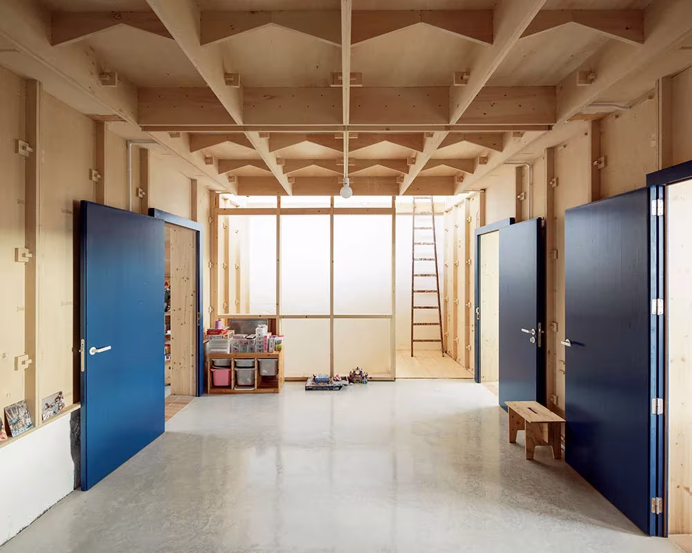 Sala diáfana con puertas azules y techo de nervios de madera contrachapada en la Plywood House de Feina
