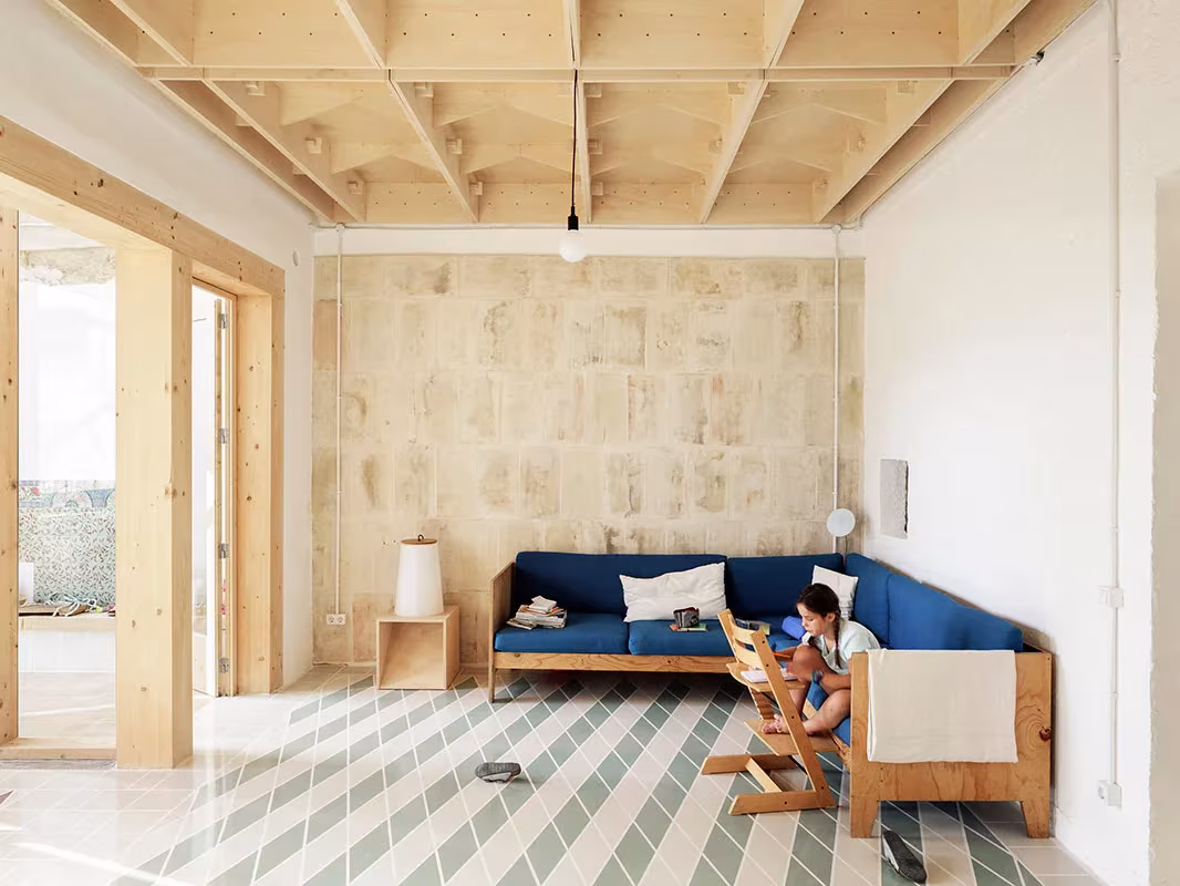 Salón de la Plywood House con sofá azul, muro de piedra clara y techo de madera en Palma