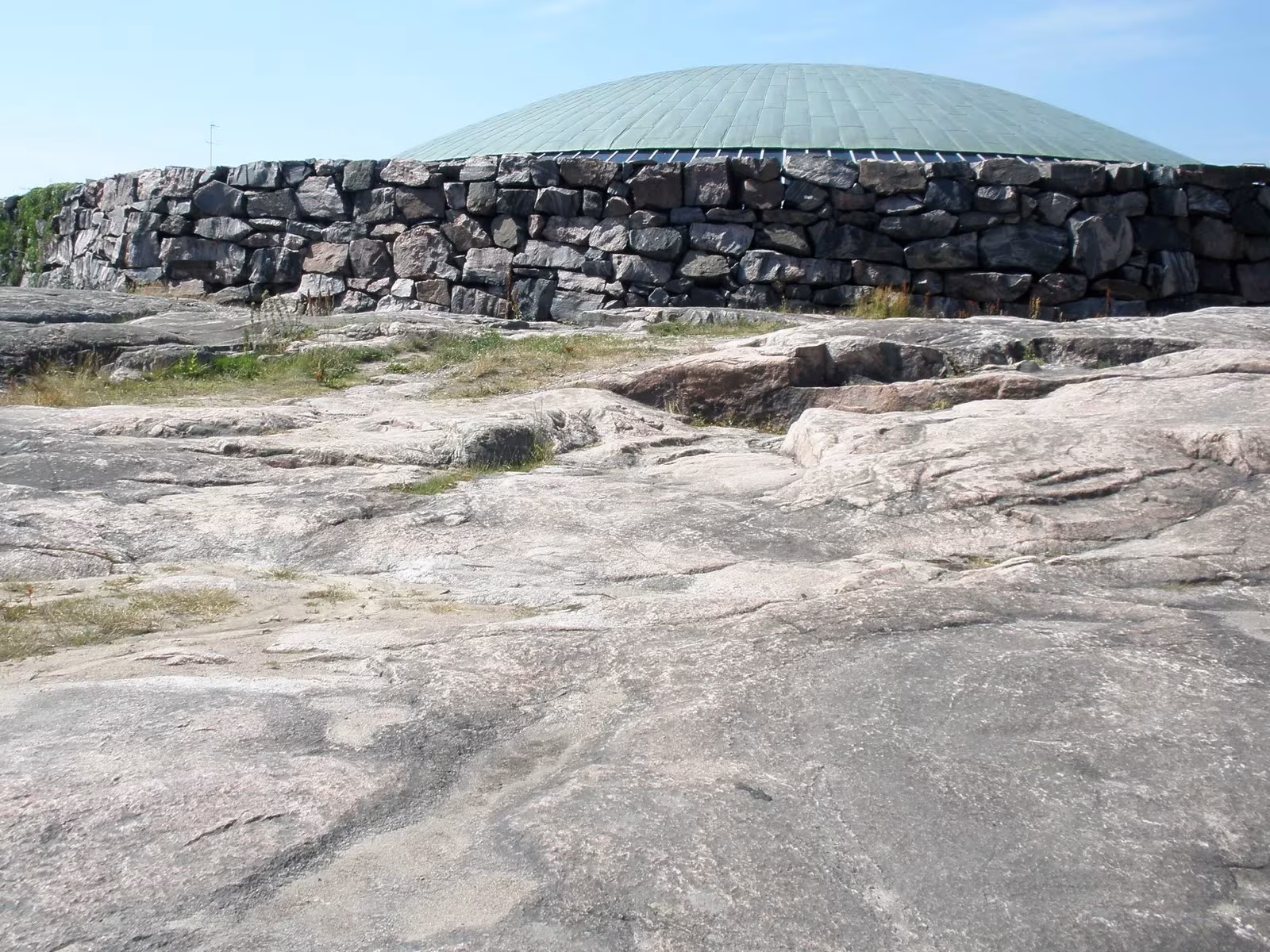 Afloramiento de granito con el muro de piedra y la cúpula de Temppeliaukio al fondo, Helsinki