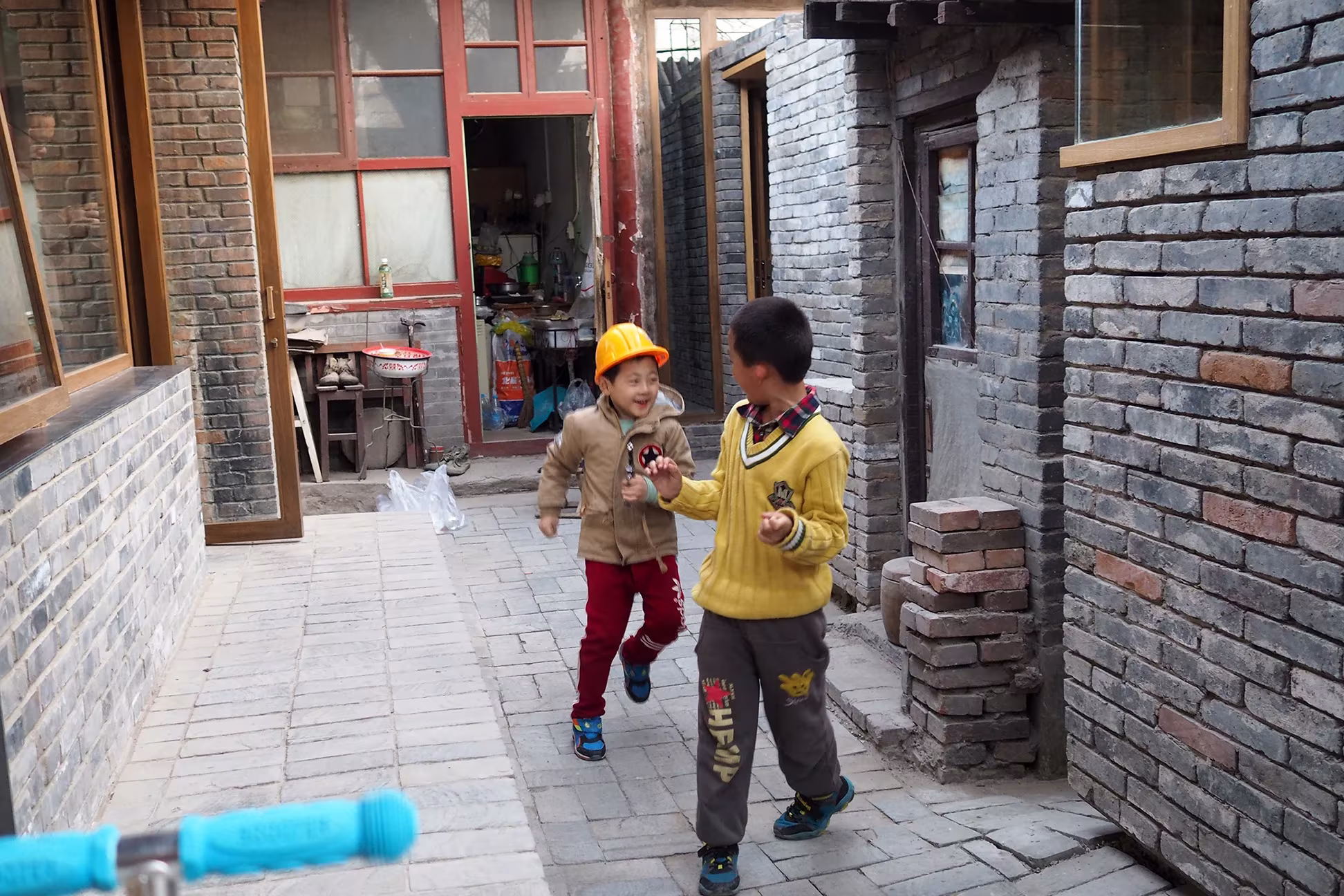 Niños jugando en un callejón del hutong con muros de ladrillo gris cerca de Tiananmen