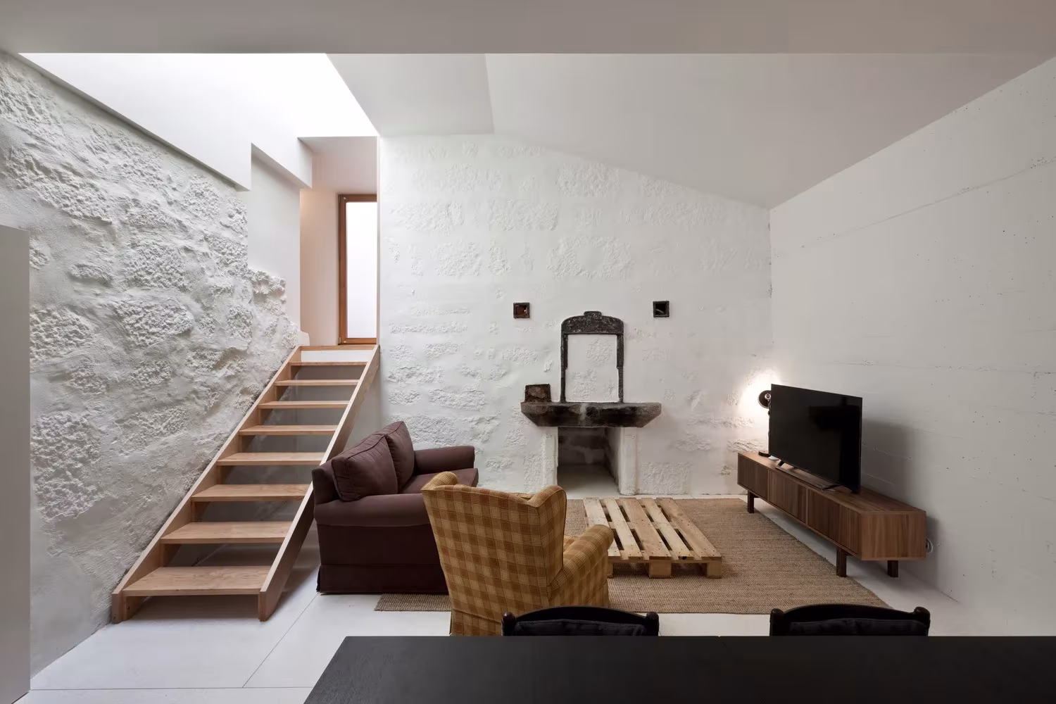 Sala de estar con muro de piedra y escalera de madera en la antigua panadería de la Casa de João