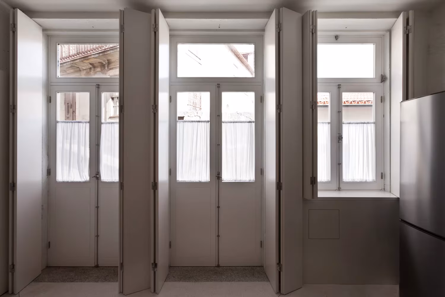 Tres ventanas con contraventanas de madera plegadas y puertas balconeras blancas en la Casa de João