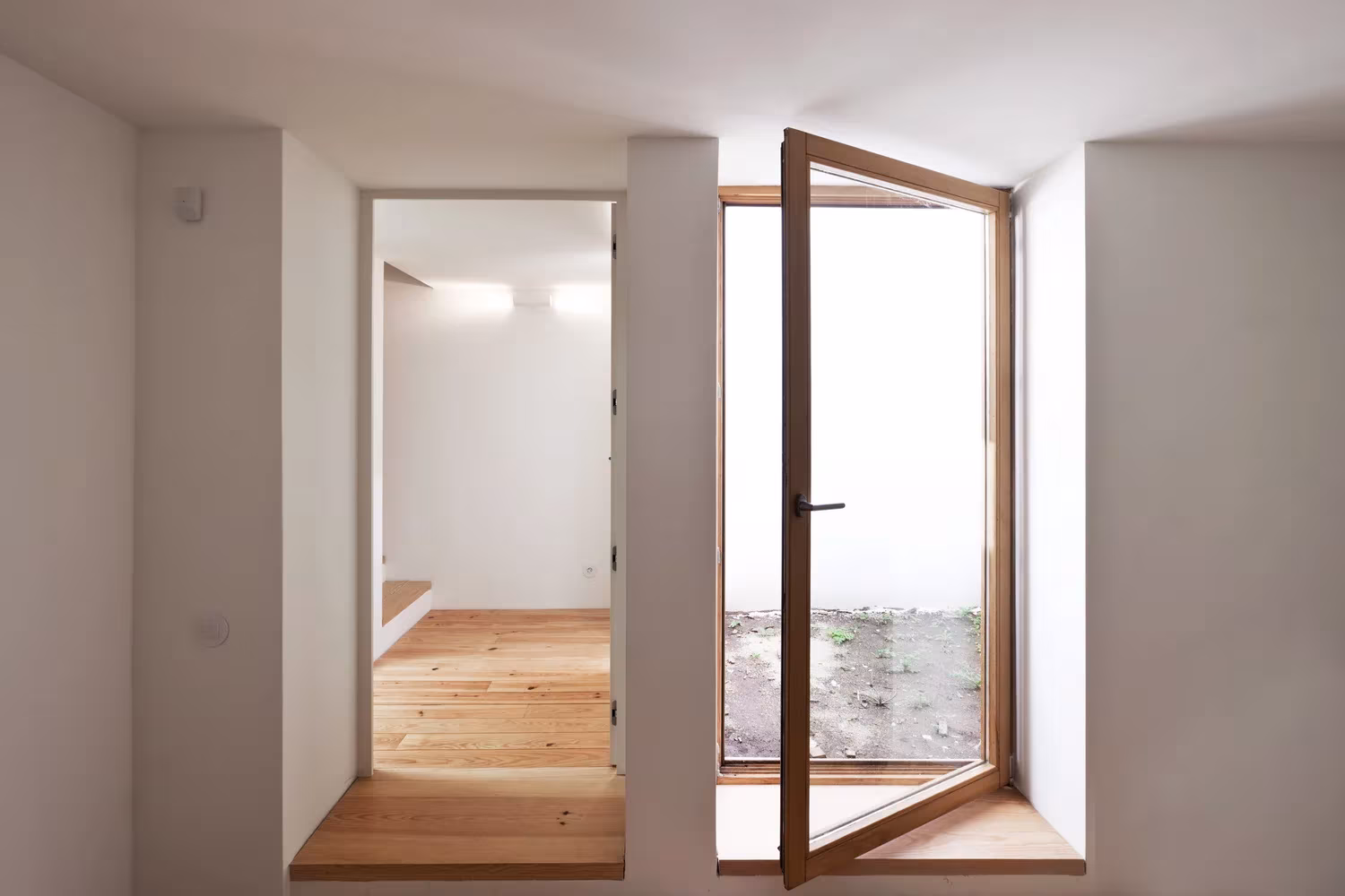 Paso blanco con ventana de madera abierta a un patio en la Casa de João, en Oporto