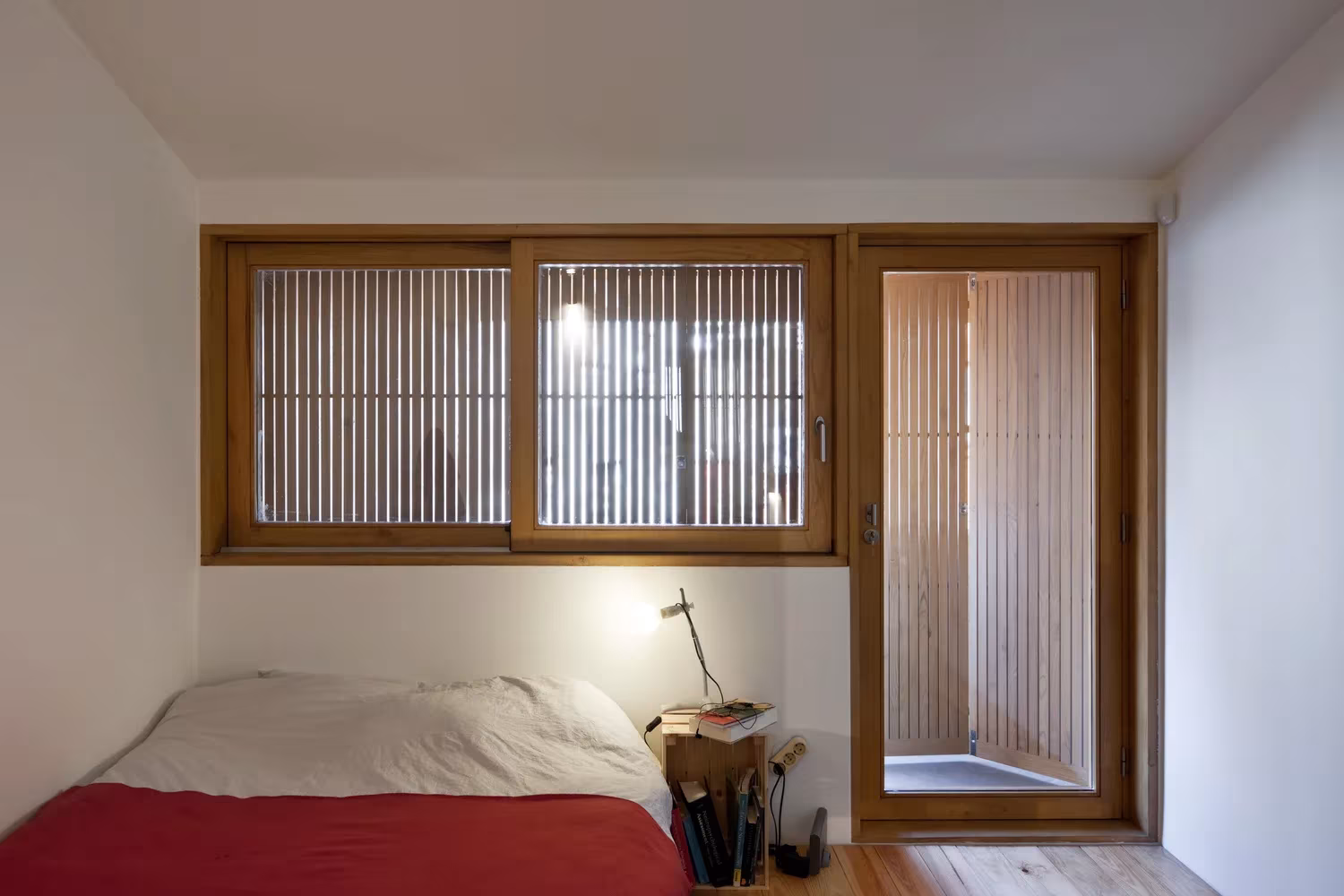 Dormitorio con ventana corredera de madera y celosía de lamas verticales en la Casa de João de Oporto