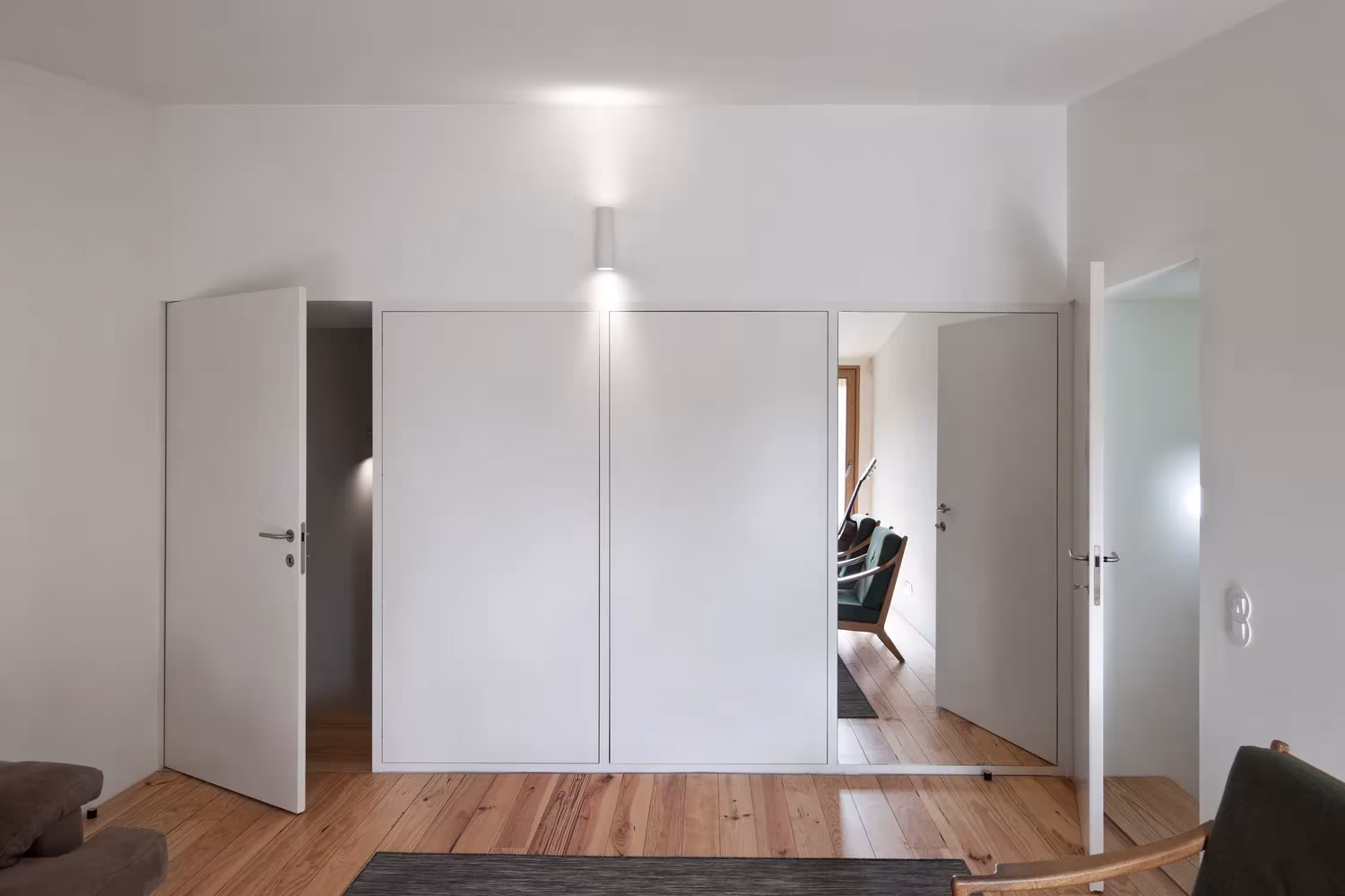 Habitación blanca con puertas lacadas abiertas y suelo de madera de pino en la Casa de João