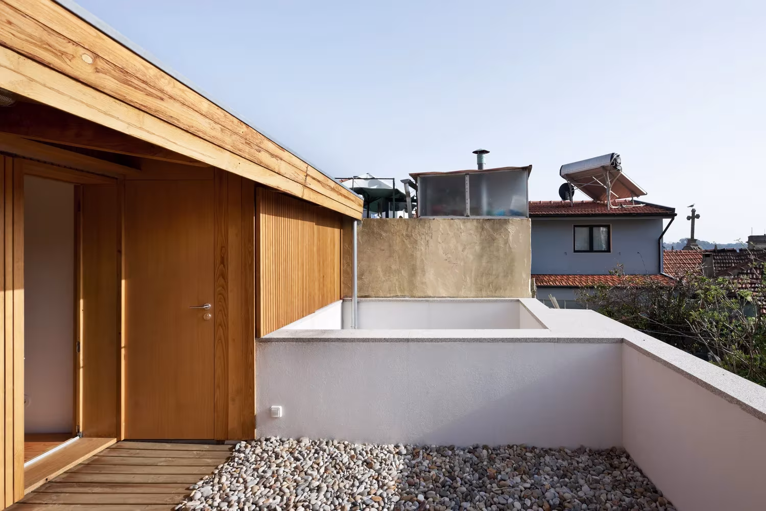 Terraza de grava con cubierta de madera y puertas de madera clara en lo alto de la Casa de João