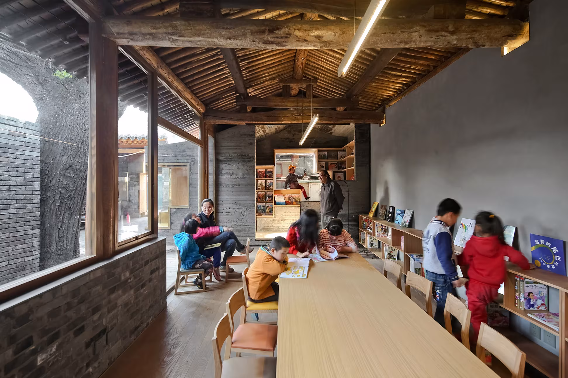 Niños sentados ante una larga mesa de madera en la biblioteca infantil del hutong, Pekín