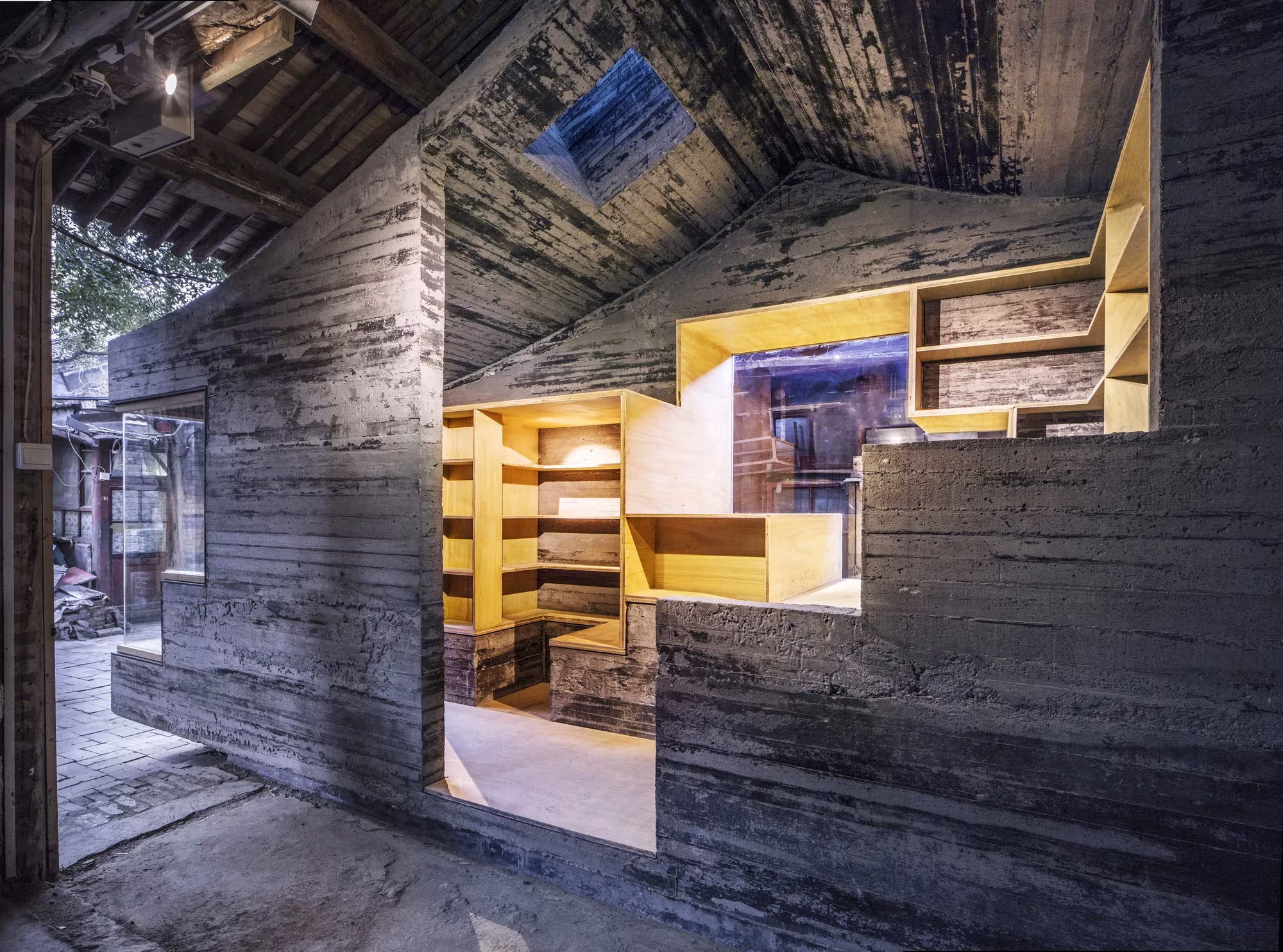 Minibiblioteca de hormigón con encofrado de madera y estanterías amarillas en un hutong de Pekín