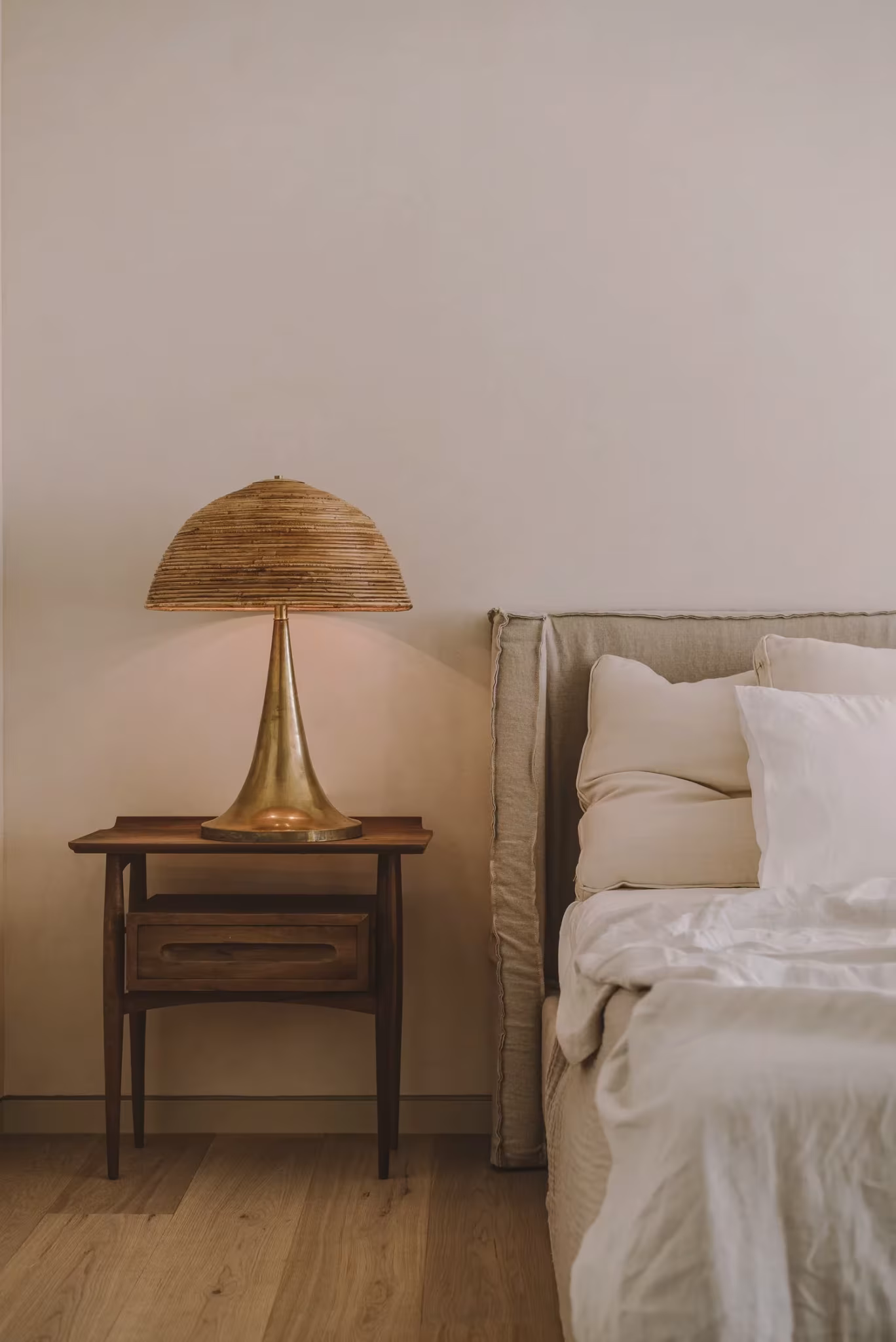 Lámpara de mimbre sobre una mesilla de madera junto a una cama de lino en la PDM House
