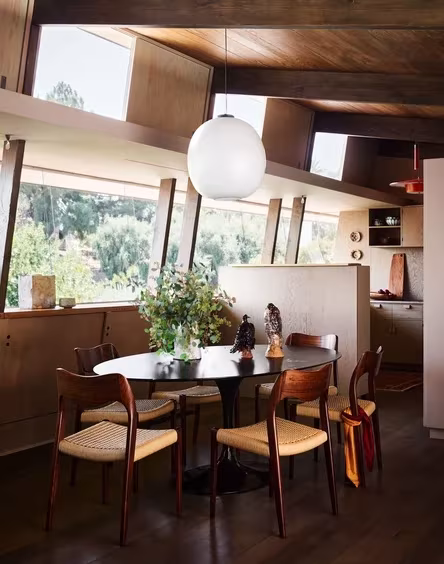 Comedor de la Pilot House con ventanales inclinados, lámpara esférica y sillas de madera en Los Ángeles