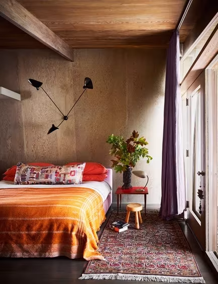 Dormitorio revestido de contrachapado con ventana alta y manta naranja en la Pilot House de Los Ángeles