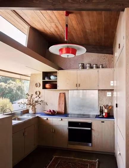 Cocina con armarios de madera clara y lámpara roja bajo un techo inclinado en la Pilot House