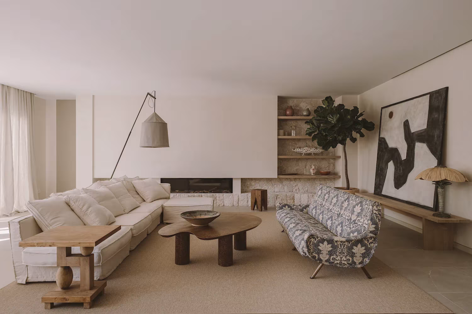 Salón con sofá blanco, mesas de madera y chimenea de piedra en la PDM House, villa de Palma