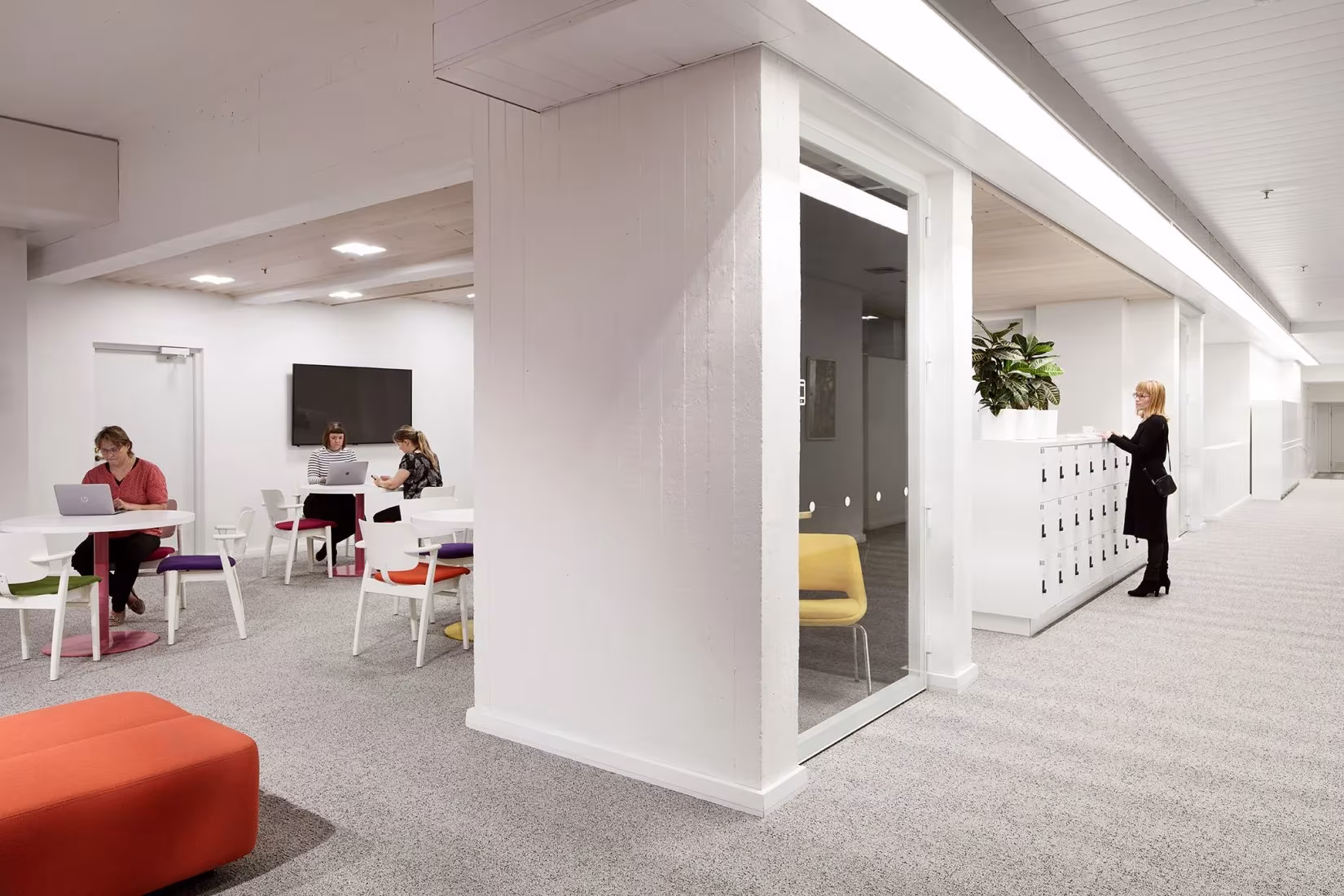 Zona de trabajo con mesas, taburetes de colores y pilares blancos en Dipoli, Universidad Aalto