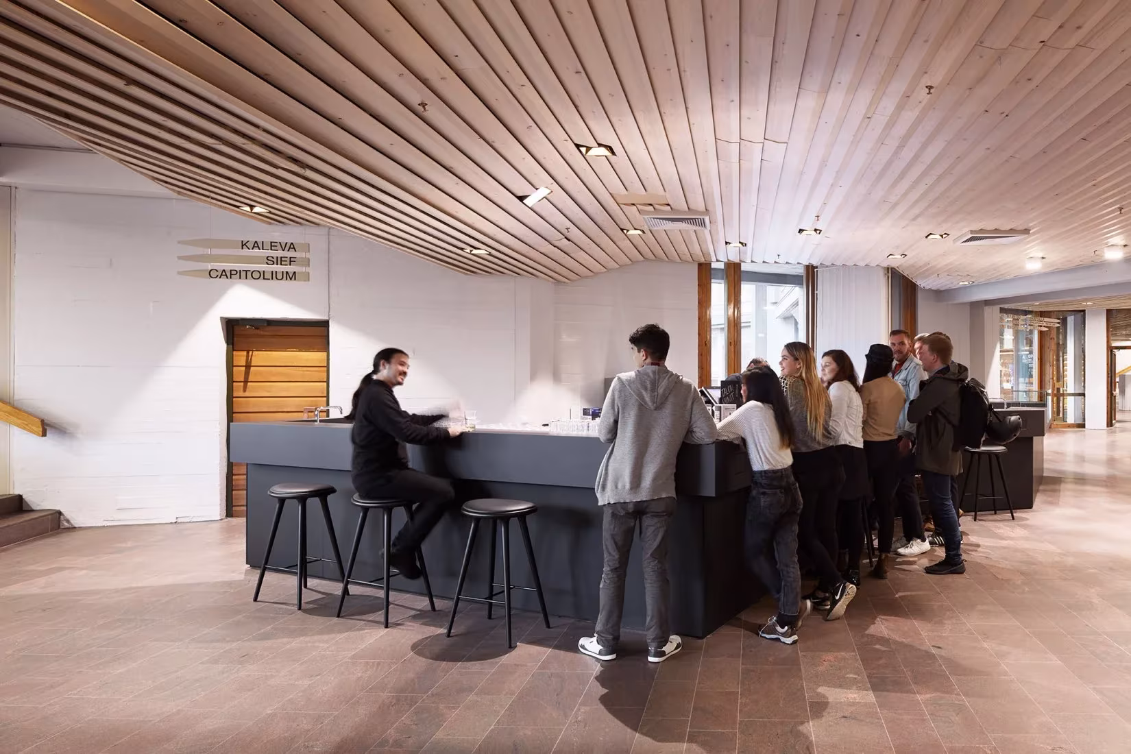 Barra de cafetería con estudiantes bajo un techo de lamas de madera en Dipoli, Finlandia