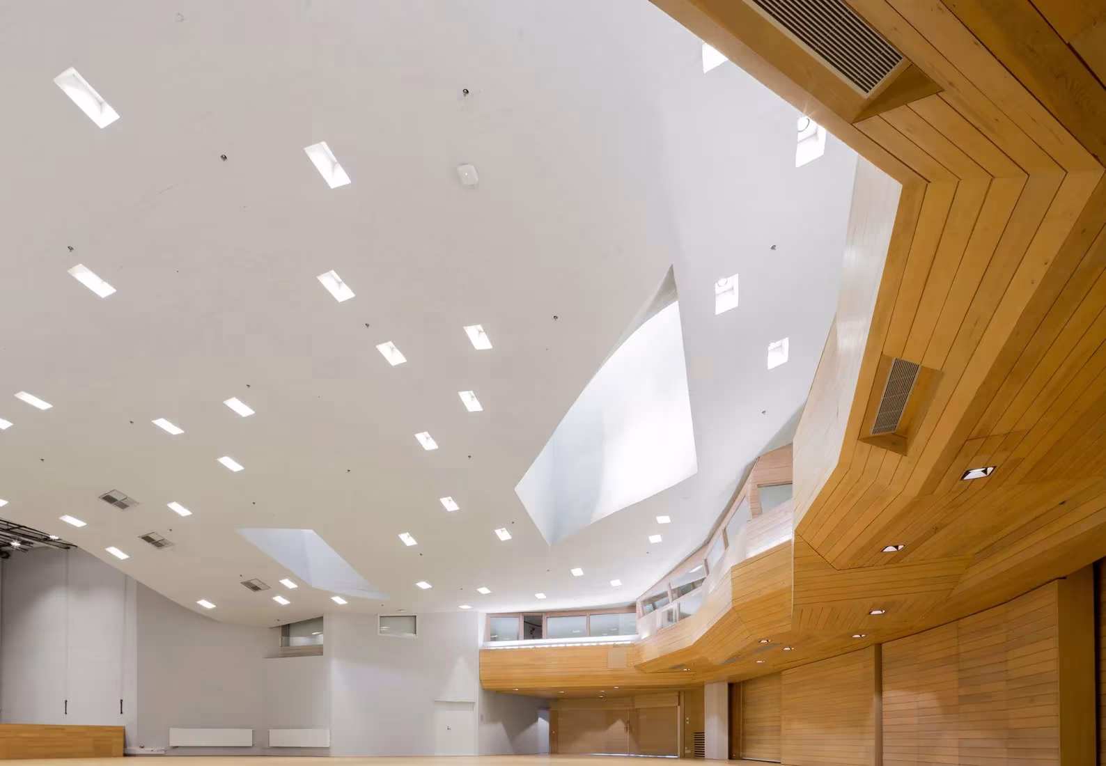 Espacio blanco con claraboyas y gran barandilla curva de madera en Dipoli, renovado por ALA Architects