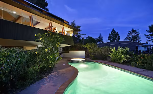 Piscina de forma orgánica iluminada al anochecer bajo la Pilot House de Jones y Smith en Los Ángeles
