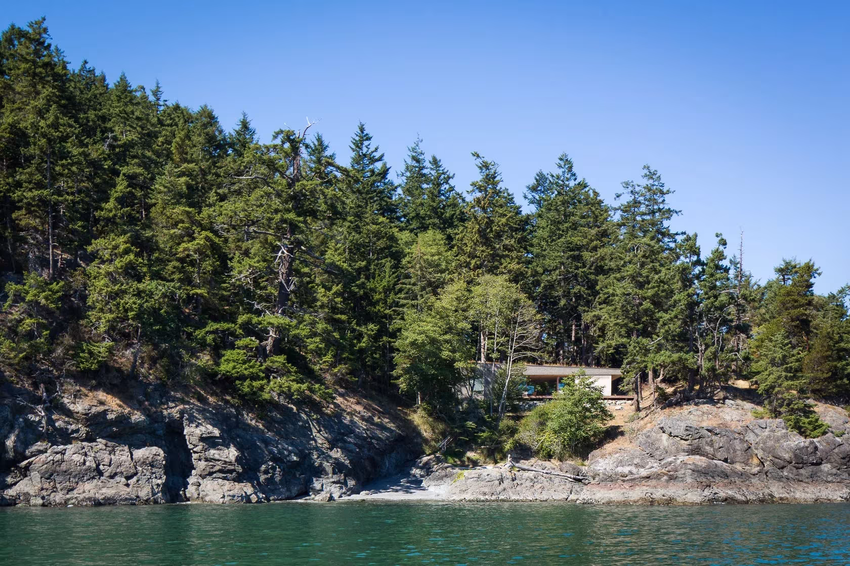 Casa Lone Madrone escondida entre abetos sobre la costa rocosa de la isla Orcas, frente al agua
