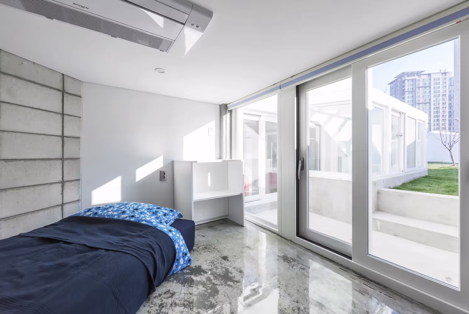 Dormitorio con cama azul y cristalera corredera al jardín en la Casa voladora de IROJE KHM Architects