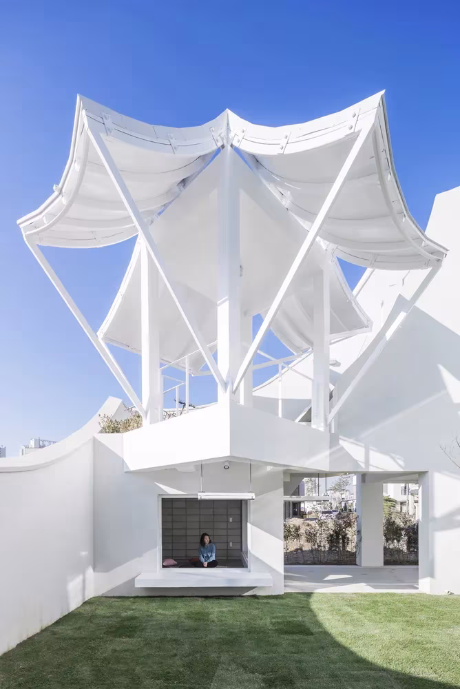 Cubierta blanca en forma de pétalos sobre el patio de césped de la Casa voladora de IROJE KHM Architects