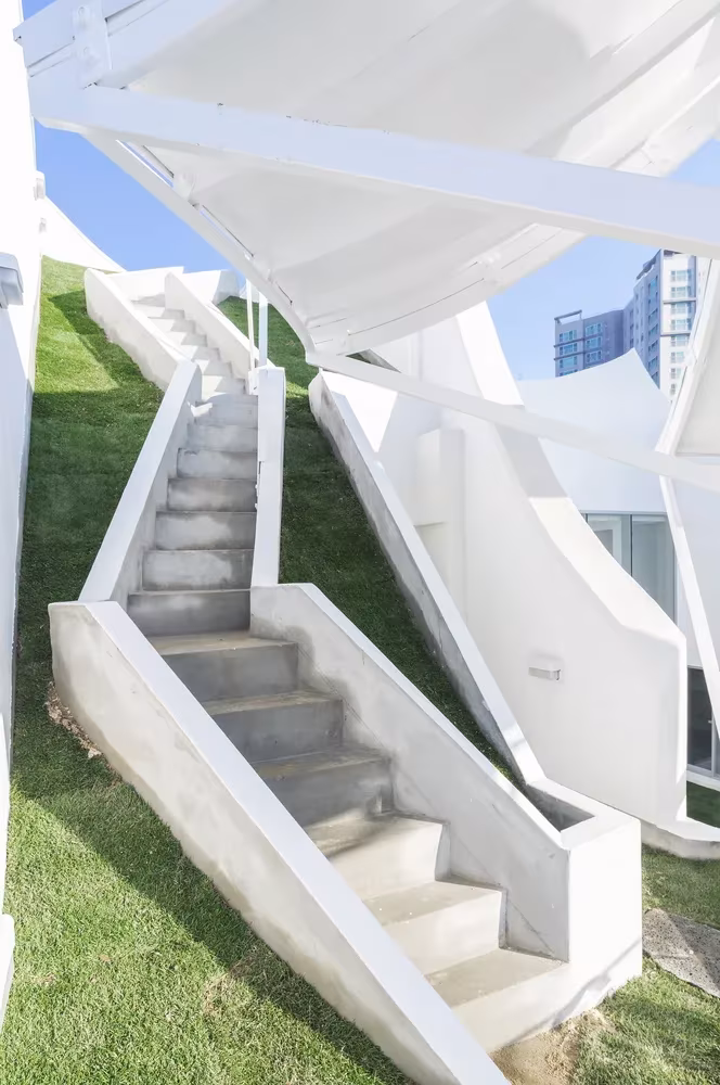 Escalera de hormigón sobre cubierta de césped bajo láminas blancas de la Casa voladora de IROJE KHM