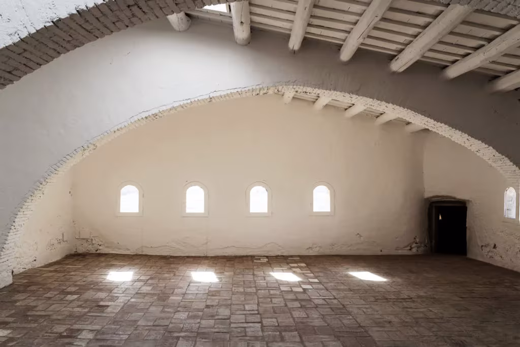 Sala con arco rebajado, techo de vigas de madera y pequeñas ventanas en el Palau de Casavells