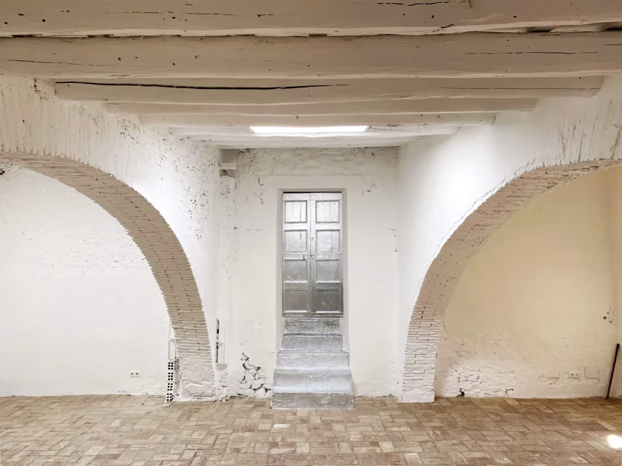 Sala con arcos de ladrillo encalados, vigas de madera y puerta al fondo en el Palau de Casavells, Corçà