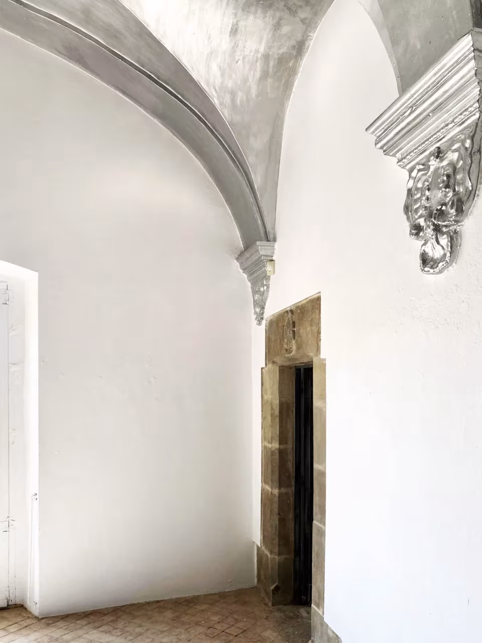 Esquina de sala encalada con bóveda plateada y puerta de piedra en el Palau de Casavells, Corçà