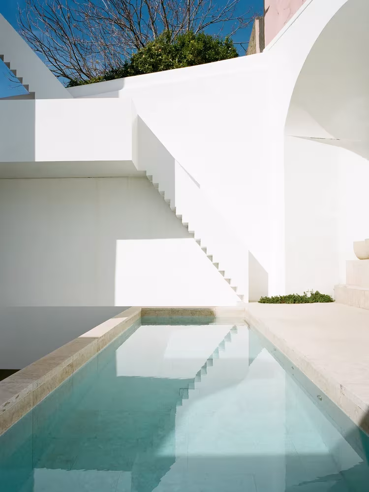 Piscina estrecha de piedra bajo una escalera blanca y un arco en el patio del Atelier Cecílio de Sousa