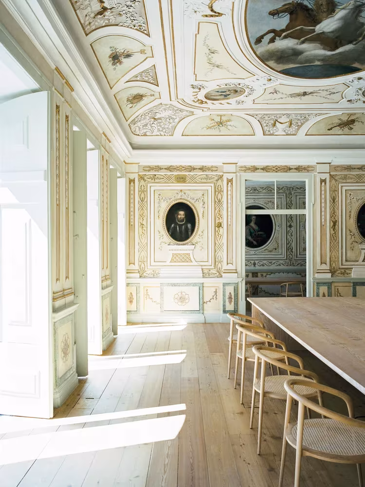 Sala con frescos y estucos, mesa corrida de madera y sillas de aro en el estudio de Aires Mateus en Lisboa