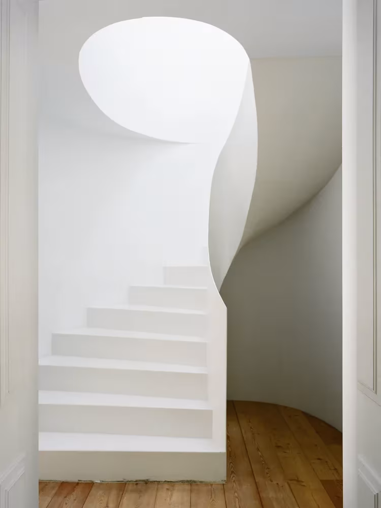 Escalera helicoidal blanca escultórica sobre suelo de madera en el estudio de Aires Mateus, Lisboa