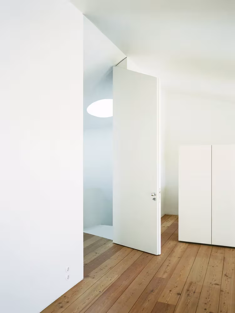 Sala blanca con suelo de tablas de madera y puerta de gran formato en el estudio de Aires Mateus, Lisboa