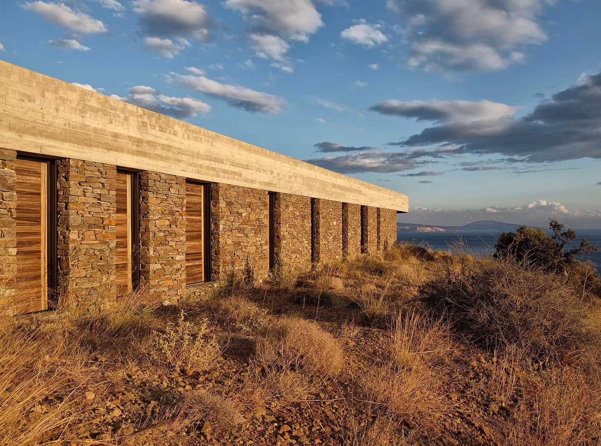 Fachada de piedra local con contraventanas de madera y cubierta de hormigón de la Ring House, en Creta