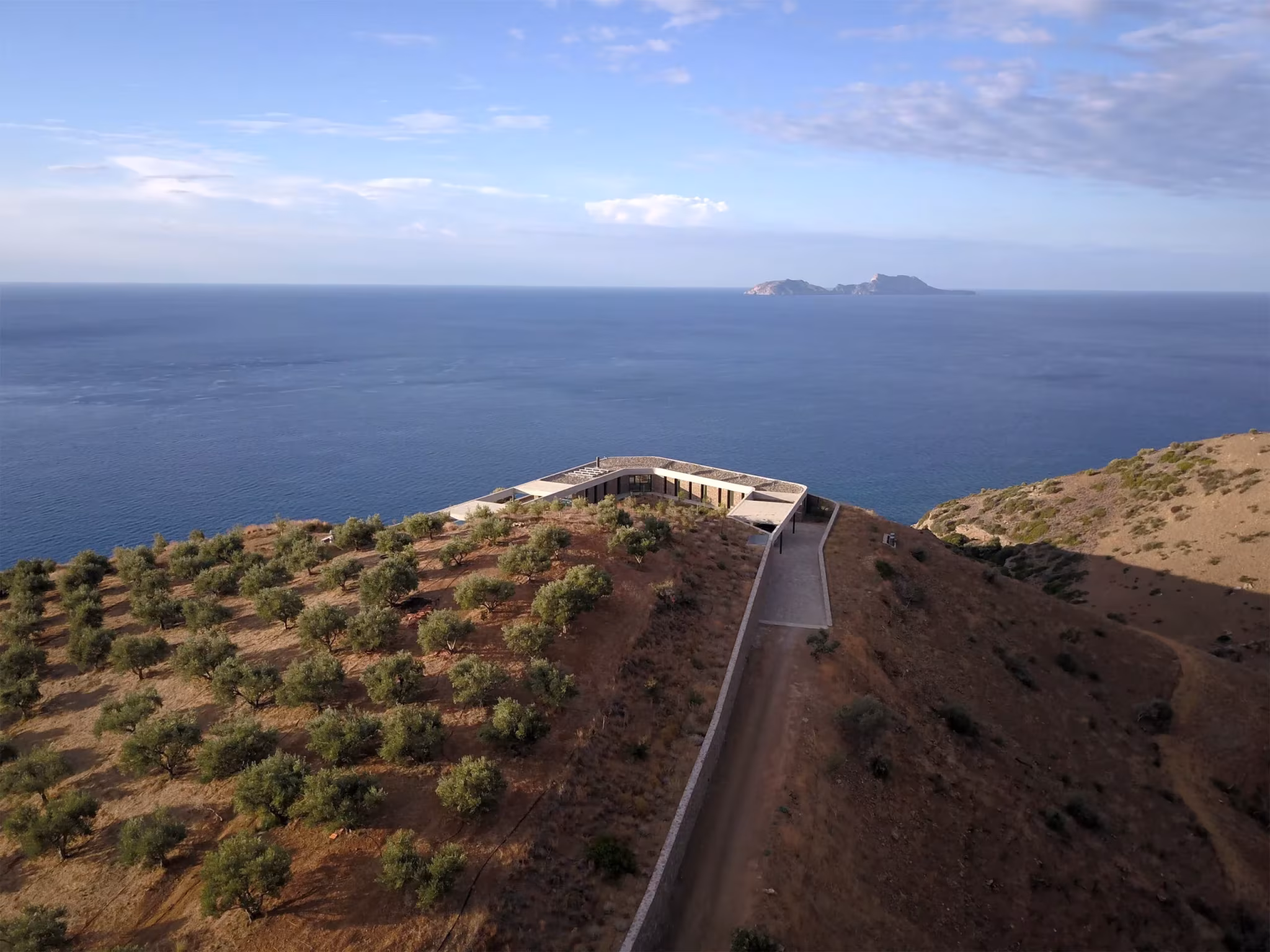 Camino de acceso y cubierta de la Ring House entre olivos, con el mar y los islotes al fondo, Creta