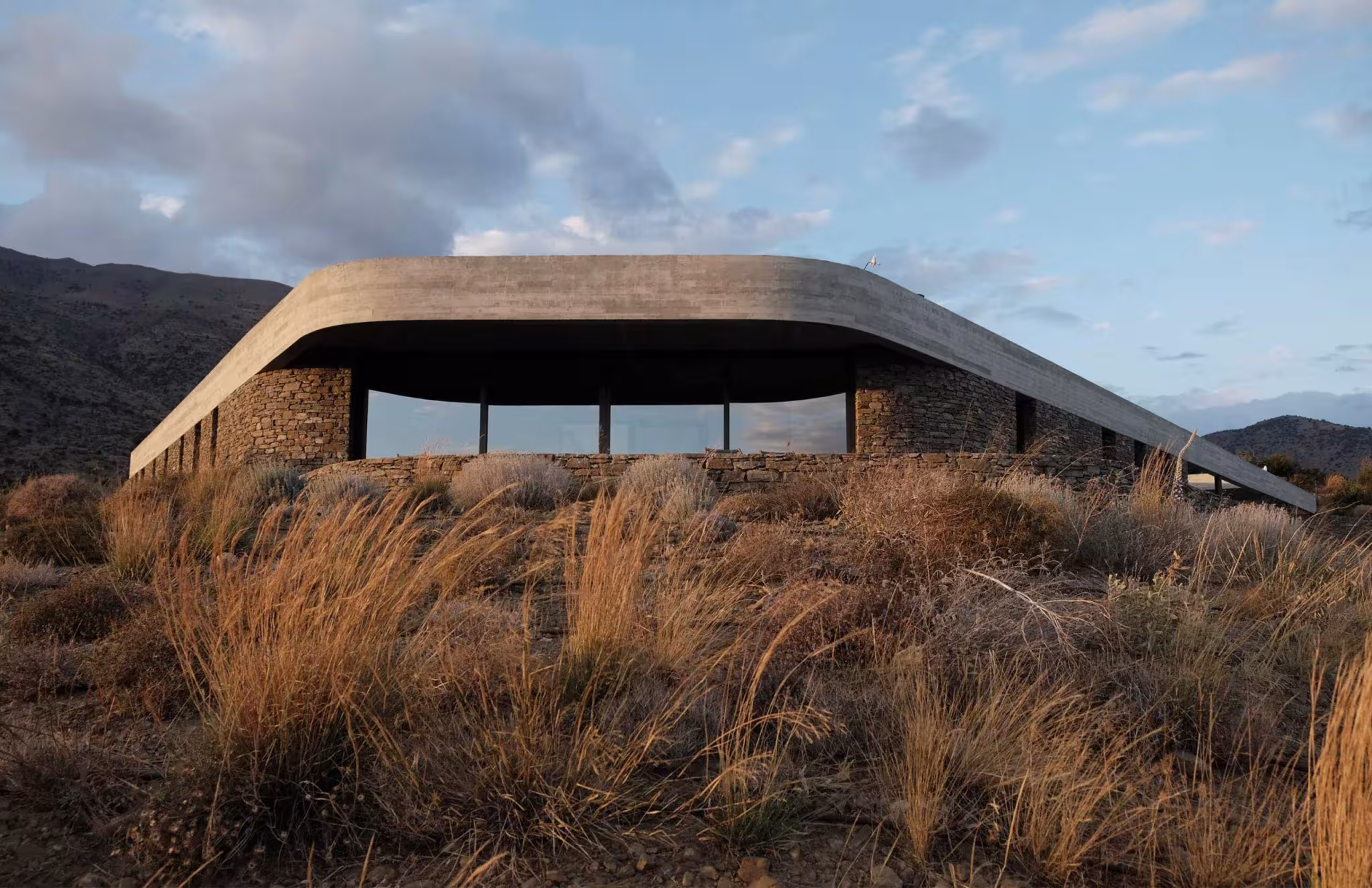 Cubierta curva y ligera de la Ring House de DECA Architecture asomando entre la vegetación seca de Creta