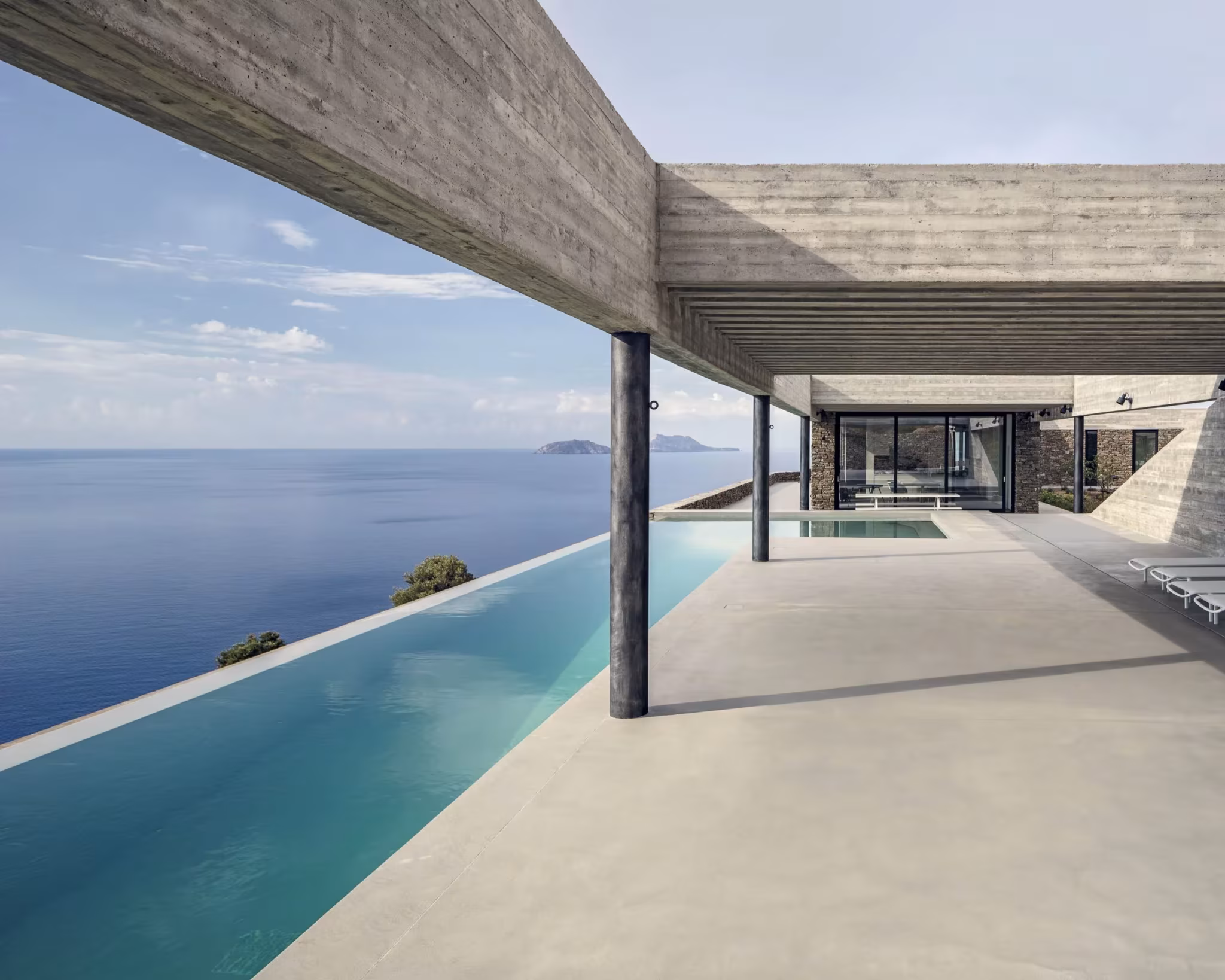 Terraza de hormigón con piscina desbordante frente al mar bajo el voladizo de la Ring House, en Creta